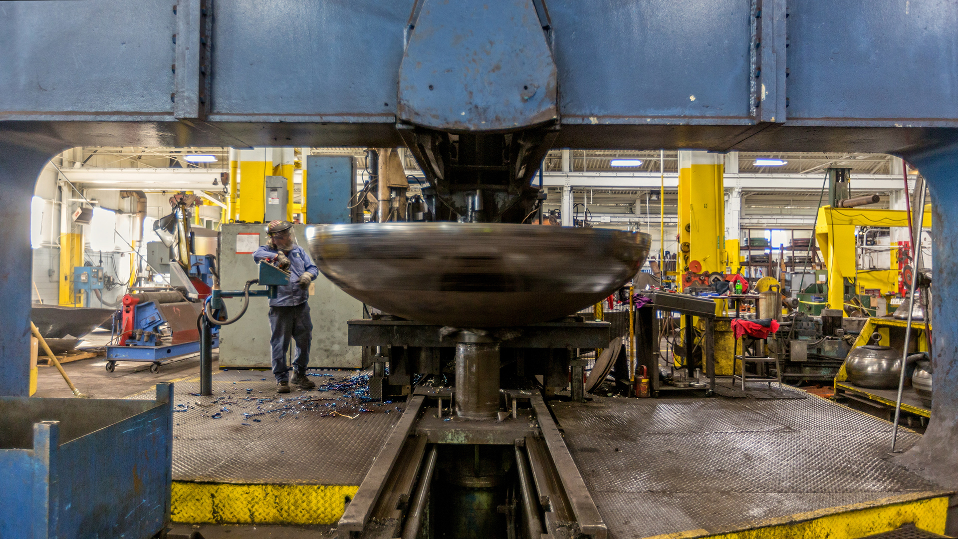 Heavy machine flanging vessel heads inside a fabrication shop.
