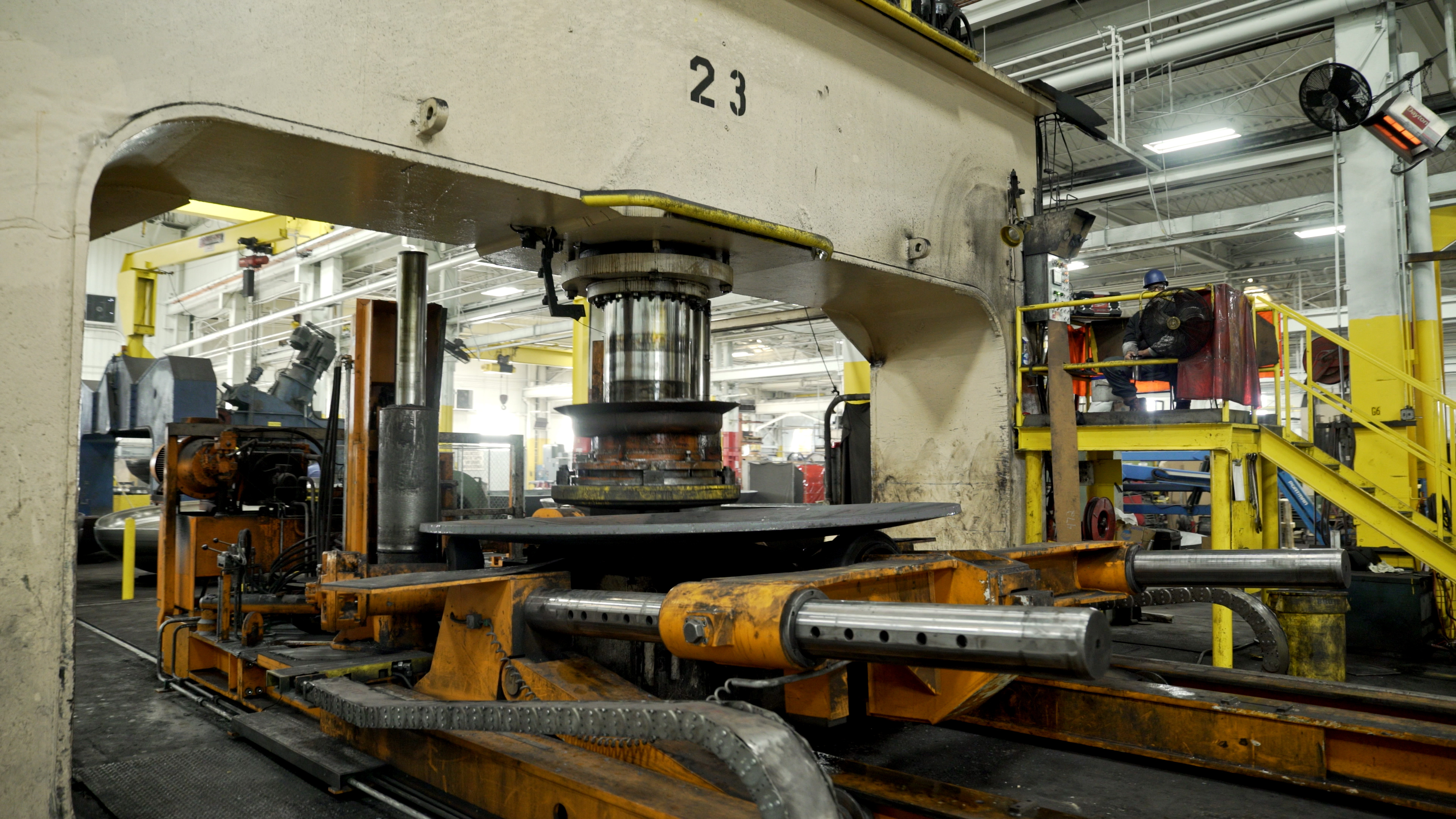 Heavy machine pressing vessel heads inside a fabrication shop.